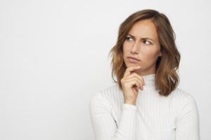 Woman wearing a white sweater looking to the side with her finger on her chin as if in thought